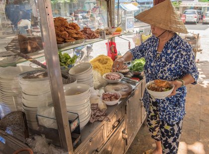 Local cart food vendor preparing a bowl of rice vermicelli in Ho Chi Minh City, Vietnam as seen on an Intrepid Travel tour.