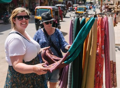 Travellers looking at locally made pashmina scarves on a busy street in Udaipur, India