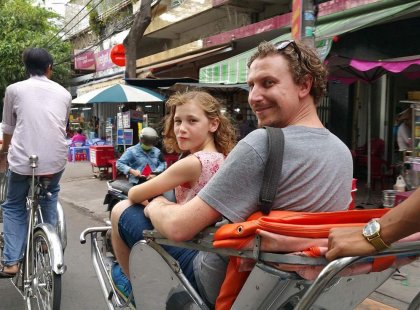 Father and daughter travelling on a rickshaw down a busy Hanoi street on an Intrepid Travel tour.