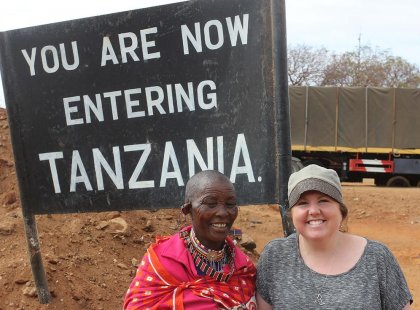 Traveller in front of a sign indicating the border from Kenya to Tanzania on an Intrepid Travel tour
