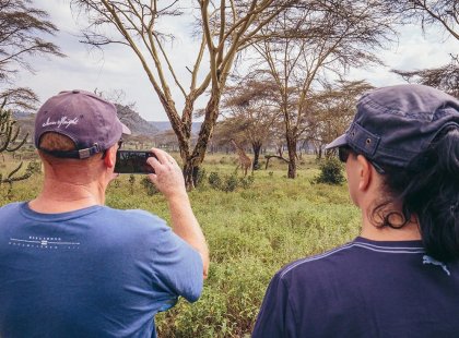 Traveller taking a photo of giraffe on his phone in Lake Naivasha National Park, Kenya on an Intrepid Travel tour