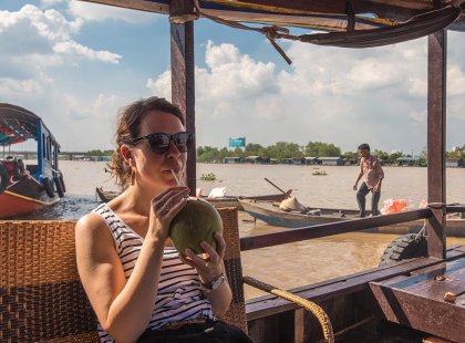Traveller taking in the sights of the Mekong River via river cruise while drinking from a fresh coconut on an Intrepid Travel Tour.