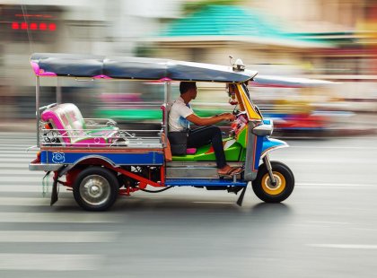 Colourful tuk-tuk zipping in between traffic on a busy Bangkok streets, Thailand on an Intrepid Travel tour