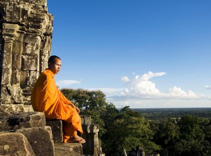 A monk sitting on the side of a temple looking out over the plush Cambodian landscape.