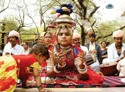 Local performer in bright red costume balancing multiple bowls on her head in Rajasthan, India