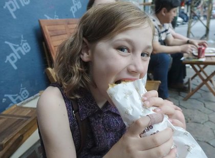 Girl eating banh mi, a local street food, outside the restaurant in Hoi An, Vietnam on an Intrepid Travel tour.