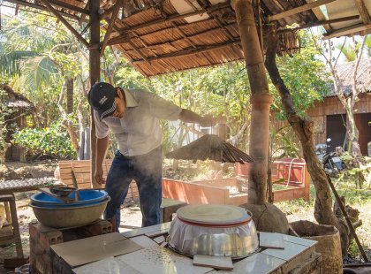 Local man demonstrating traditional cooking technique in a village along the Mekong River, Vietnam on an Intrepid Travel tour.