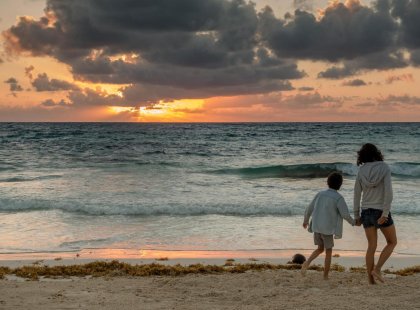 Mother and ten year old son walk on the beach during sun set in beautiful Tulum, Mexico