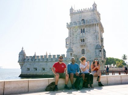 Intrepid travellers sitting on river bank in front of Belem Tower, Lisbon, Portugal