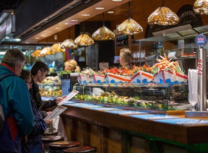 Travellers looking at delicious food options in a local stall at a market in Barcelona, Spain.