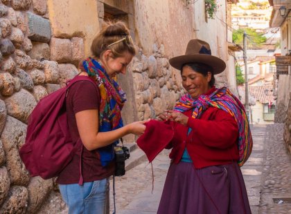 Local woman dressed in traditional attire helping a traveller with their hat in Cusco, Peru