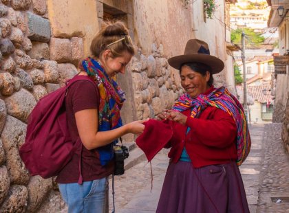 Local woman dressed in traditional attire helping a traveller with their hat in Cusco, Peru