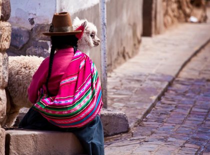 Local woman in traditional dress with alpaca on cobbled street, Cusco, Peru